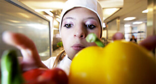 Eine Schülerin die am Berufsorientierungsprogramm des Bundesministeriums für Bildung und Forschung teilnimmt lernt den Beruf des Kochs kennen. Sie steht in einem offenen Kühlschrank und greift nach zwei Paprika.